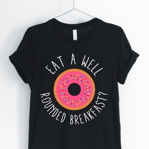 Peut inclure: T-shirt noir avec un graphique blanc d'un beignet et le texte "Eat a well rounded breakfast?"