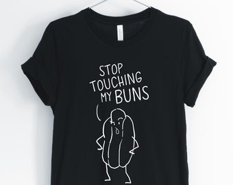 May include: Black t-shirt with a white graphic of a hot dog with arms and legs. The text "STOP TOUCHING MY BUNS" is above the hot dog.