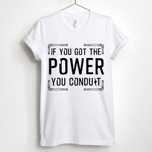 以下が含まれることがあります： 白いTシャツに黒い文字で「If you got the power you conduct」と書かれています。テキストは電気配管のグラフィックで囲まれています。