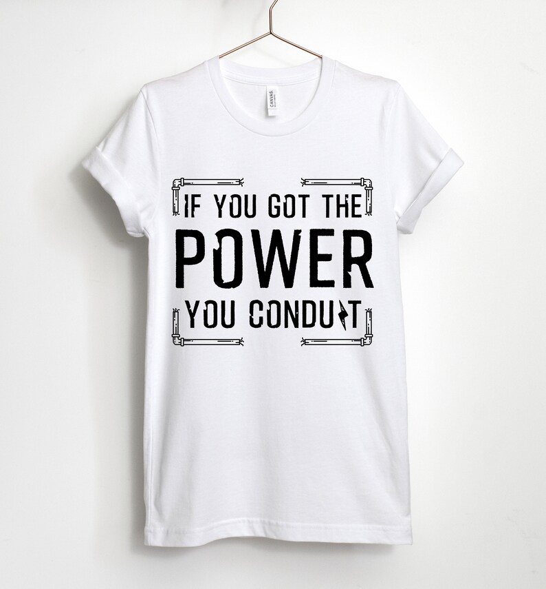 以下が含まれることがあります： 白いTシャツに黒い文字で「If you got the power you conduct」と書かれています。テキストは電気配管のグラフィックで囲まれています。