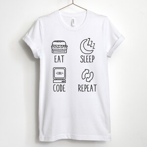 May include: White t-shirt with black text and illustrations. The text reads "Eat, Sleep, Code, Repeat". The illustrations include a hamburger, a crescent moon with zzz's, a computer with code, and a circular arrow.