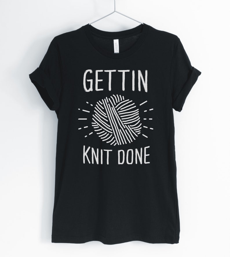 May include: Black t-shirt with white text that reads "Gettin' Knit Done" and a white illustration of a ball of yarn.