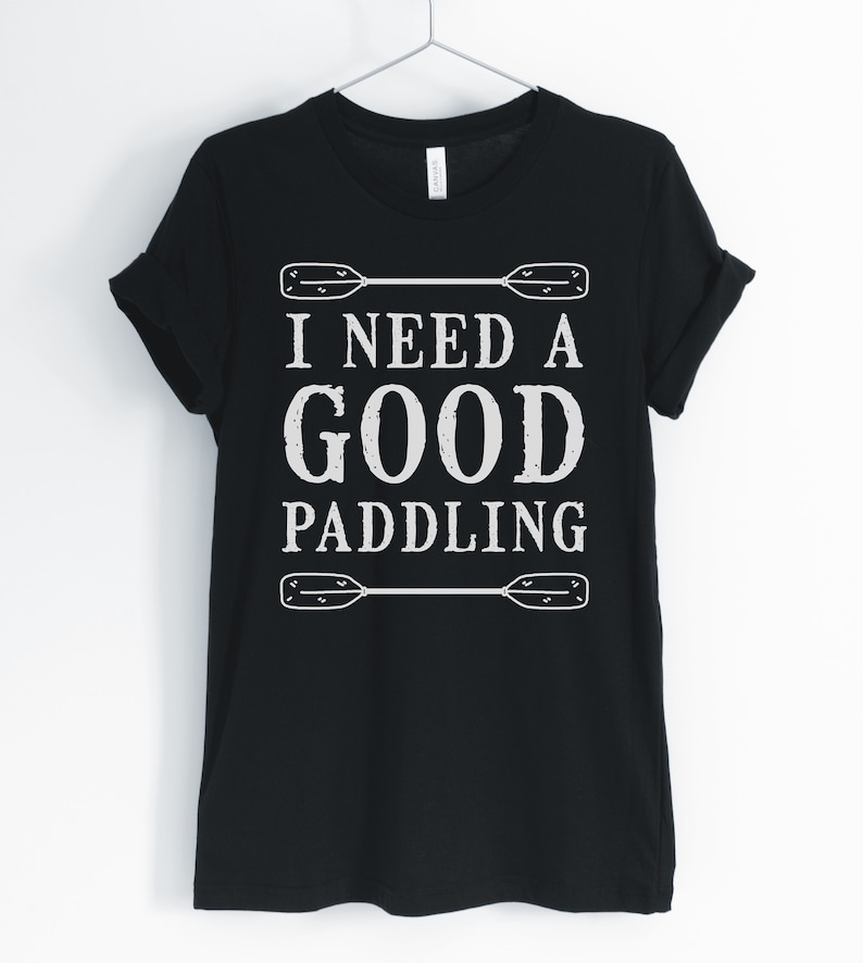 May include: Black t-shirt with white text that reads "I need a good paddling" with two white paddle oars above and below the text.
