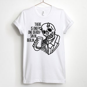 Puede incluir: Camiseta blanca con una ilustraci&oacute;n en blanco y negro de una calavera con cuernos sosteniendo un vaso de cerveza. El texto "THERE IS ONLY ONE DEADLY SIN IN BERLIN." est&aacute; impreso en la camiseta.
