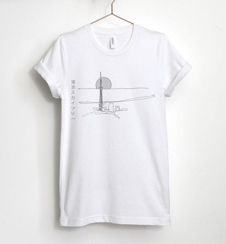 May include: White t-shirt with a line drawing of a tall building and a sun in the background. The text "東京スカイツリー" is printed on the left side of the shirt.