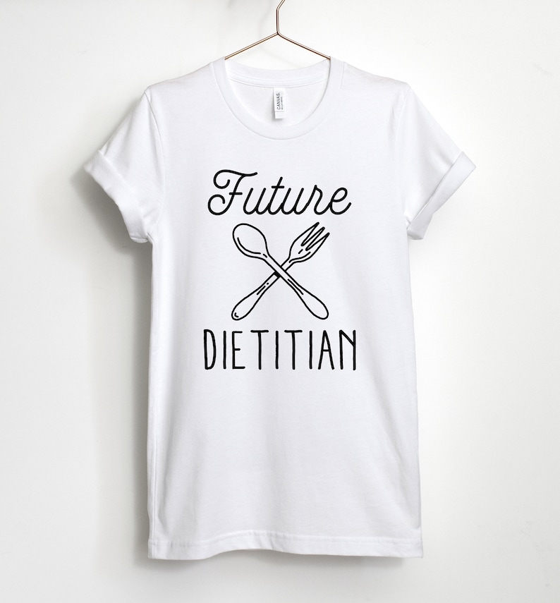 K&ouml;nnte beinhalten: Wei&szlig;es T-Shirt mit schwarzem Text "Future Dietitian" und einer Grafik einer gekreuzten Gabel und L&ouml;ffel.