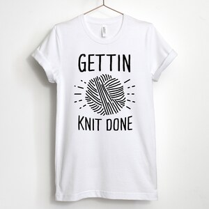 May include: White t-shirt with black text that reads "Gettin' Knit Done" and a graphic of a ball of yarn.