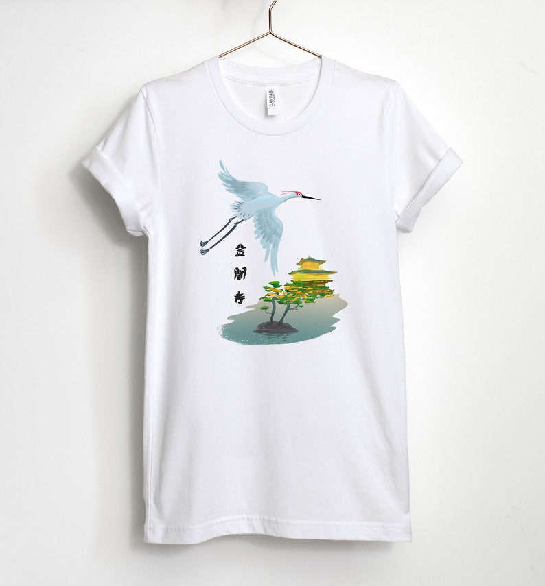 May include: White t-shirt with a graphic of a crane flying over a golden pagoda with a tree in front of it. The text "金閣寺" is written in black on the left side of the image.
