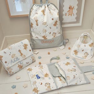 Può includere: Una collezione di accessori per bambini con un design stravagante. Il set include uno zaino con coulisse, un fasciatoio, un bavaglino e una pochette per pannolini. Ogni articolo presenta un motivo ripetuto di orsetti, giraffe ed elementi celesti in tonalità tenui e neutre.