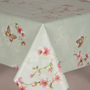Op de afbeelding: Een lichtgroen tafelkleed met een bloemen- en vlinderontwerp. Het ontwerp bevat roze kersenbloesems en bruine vlinders. De stof heeft een subtiele gestreepte textuur. Het tafelkleed is opgevouwen en toont het patroon.