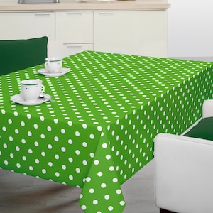 Puede incluir: Mantel de mesa verde con lunares blancos. El mantel está puesto sobre una mesa con dos tazas de café blancas y sus platillos.