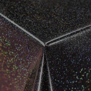 Könnte beinhalten: Schwarze Tischdecke mit einem glitzernden, schimmernden Finish. Die Tischdecke hat einen dezenten Glanz und eine strukturierte Oberfläche.