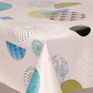 May include: White tablecloth featuring a repeating pattern of abstract shapes in blue, teal, black, and olive green. The design includes circles, spirals, and stylized botanical elements. The tablecloth is folded, showing the fabric's texture.
