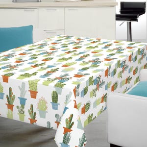 May include: A white rectangular tablecloth with a repeating pattern of potted cacti in various colours. The cacti are in orange, blue, and green pots. The tablecloth is on a rectangular table in a kitchen setting.