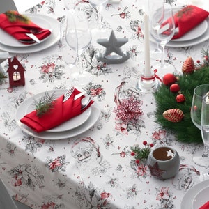 May include: White tablecloth with a Christmas theme featuring a repeating pattern of Santa Claus, holly, and berries. The tablecloth is set with red napkins, white plates, and silver cutlery. There are also decorative elements such as a star, a candle, and a wreath.