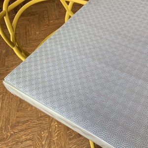 May include: A close-up of a grey table runner with a hexagonal pattern. The runner is made of a textured material and has a white border.