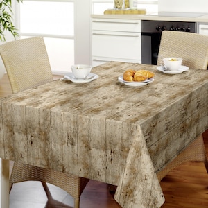 Op de afbeelding: Een rechthoekig tafelkleed met een realistische print van verweerde, lichtbruine houten planken met zichtbare nerven en verweerde texturen. De stof valt over een eettafel en zorgt voor een rustieke uitstraling met een neutraal kleurenpalet.