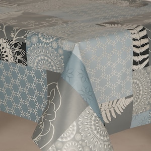 May include: A patterned tablecloth in a patchwork design, featuring various shades of grey and blue. The patterns include floral, geometric, and mandala motifs. The material appears to be smooth, possibly vinyl.