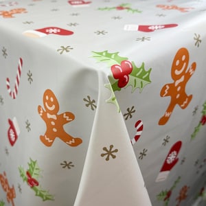 May include: A white tablecloth with a festive Christmas design featuring gingerbread men, candy canes, holly, and snowflakes.