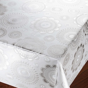 Könnte beinhalten: Eine silberne Tischdecke mit einem sich wiederholenden Muster aus stilisierten floralen Medaillons. Das Design ist geprägt und erzeugt eine strukturierte Oberfläche. Die Tischdecke besteht aus einem glänzenden, reflektierenden Material und eignet sich für einen Esstisch.