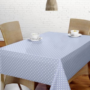 May include: A pale blue tablecloth with white polka dots covers a table. Two wicker chairs flank the table, set for a meal. A woven pendant light hangs above the table, creating a warm ambiance.