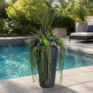May include: A tall, dark grey planter filled with a variety of faux greenery and succulents. The arrangement includes long, trailing vines, spiky leaves, and colourful purple and green accents. The planter sits by a pool.
