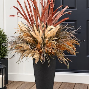 May include: A tall, matte black tapered planter filled with an arrangement of dried botanical elements. The display features upright rust-coloured leaves, fluffy cream-coloured plumes, and wispy dark brown foliage, creating a dense, textured bouquet.
