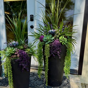 Peut inclure: Deux grands pots coniques noir mat remplis de verdure artificielle. Les compositions présentent de longues herbes vertes pointues, des plantes succulentes vert clair, des grappes de fleurs violettes et des vignes tombantes sur les côtés.