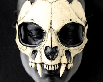 Könnte beinhalten: Eine weiße Totenkopfmaske mit scharfen Zähnen und schwarzen Augenhöhlen. Die Maske ist aus hartem Kunststoff gefertigt und wirkt realistisch.