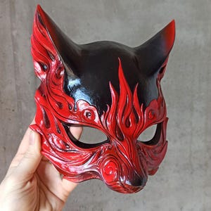May include: A red and black fox mask with intricate details. The mask is made of leather and has a glossy finish. The mask is shaped like a fox's head with pointed ears and a long snout.