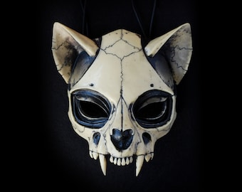 Könnte beinhalten: Eine weiße und schwarze Katzen Schädelmaske mit detaillierter Knochenstruktur und scharfen Zähnen. Die Maske hat schwarze Augenhöhlen und eine schwarze Nase.