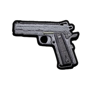 May include: Embroidered patch featuring a detailed gray handgun design. The patch has a black border and showcases the intricate details of the firearm, including the slide, grip, and trigger. The patch is suitable for jackets, bags, or other fabric items.