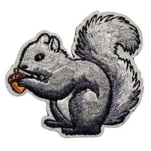 May include: Embroidered patch featuring a gray squirrel holding a brown acorn. The squirrel has a fluffy tail and is set against a white background. The patch has a gray border.