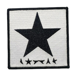 May include: Square patch with a white background and a large black star in the center. Below the star are three smaller black star shapes. The patch has a black border.