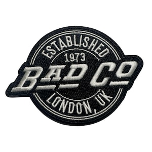May include: A black and white patch with the text "BAD CO" in bold, outlined white letters. The patch is circular with the words "ESTABLISHED 1973" and "LONDON, UK" in a circular pattern around the central text.