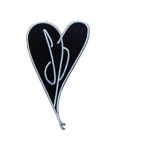 May include: Black heart-shaped embroidered patch with a white border and white cursive initials "SB" in the center. The patch has a smooth texture and is set against a white background. Ideal for jackets, bags, or other fabric items.