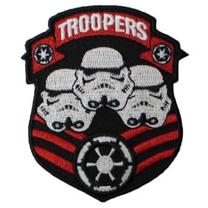 May include: Embroidered patch featuring three white Stormtrooper helmets on a black shield. The word "TROOPERS" is arched across the top in white on a red banner. A red and black design is at the bottom.