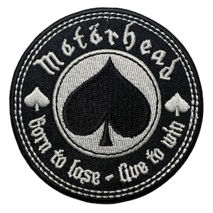 May include: Black and white embroidered patch with the text "Motörhead" above a black spade symbol. The phrase "born to lose - live to win" is written around the spade. The patch has a white stitched border.