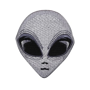 May include: A gray alien patch with large black oval eyes and a small mouth. The patch has a textured appearance and a dark blue outline around the eyes. The alien's head is oval-shaped.
