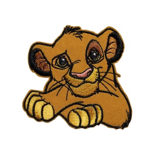 May include: Embroidered patch featuring a smiling lion cub with a golden-yellow body, black-tipped ears, and a pink nose. The patch has a detailed design with visible stitching and is set against a white background.