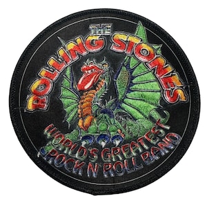 May include: Round black patch featuring a dragon with green wings and an orange body. The text "THE ROLLING STONES" arches across the top in red, orange, and yellow. Below the dragon, the text reads "WORLD'S GREATEST ROCK N ROLL BAND."