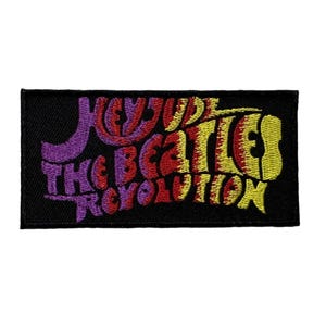 May include: A rectangular black embroidered patch featuring the words "Hey Jude The Beatles Revolution" in a colorful, psychedelic font. The text is in purple, red, and yellow. The patch is likely for a jacket or bag.
