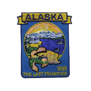 May include: Embroidered Alaska patch with a blue background. The patch features a circular design with a mountain range, lake, and fish. The text "ALASKA" is at the top, and "THE LAST FRONTIER" and "1959" are at the bottom.