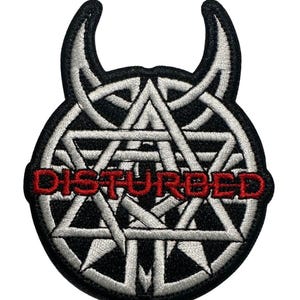 May include: Embroidered patch featuring the word "DISTURBED" in red, set against a white geometric design within a black outline. The patch has a unique shape with two curved horns at the top, suitable for jackets or bags.