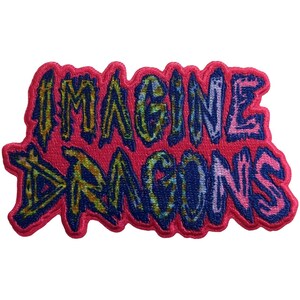 May include: An embroidered patch featuring the text Imagine Dragons in a stylized, jagged font. The lettering displays a gradient of yellow, blue, and pink hues, set against a solid, vibrant pink background that follows the contour of the letters.