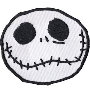 May include: A white embroidered patch featuring the face of Jack Skellington from The Nightmare Before Christmas. The design includes large black eyes, a stitched mouth, and a black outline.