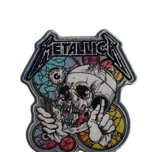 May include: Embroidered patch featuring a detailed skull design with colorful elements and the band name "METALLICA" in silver lettering. The patch has a gray border and is likely for jackets or bags.