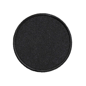 May include: A round, black patch with a textured surface and a stitched border. The patch is a solid color and appears to be made of fabric. The patch is circular and could be used for clothing or accessories.