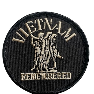 May include: A circular black embroidered patch with the word "VIETNAM" arched across the top in tan thread. Below, a tan image of soldiers is centered, with the word "REMEMBERED" below.