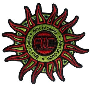 May include: Embroidered patch featuring a stylized sun design in red, green, and black. The sun's rays are red with green accents, surrounding a green circle with the text "Alice in Chains." The band's logo is in the center.